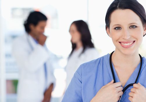 Young smiling nurse standing upright accompanied by her team who is standing behind her