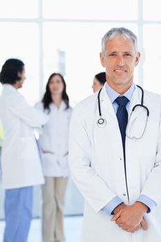 Doctor smiling while his team is talking in the background