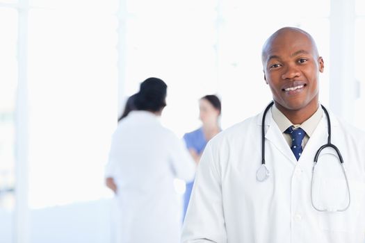 Doctor standing in a well-lit room with his team in the background