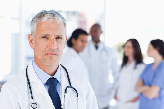 Mature doctor looking straight ahead with a serious look on his face while his team is behind him