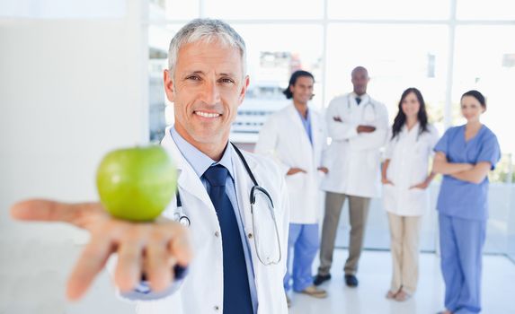 Medical interns in the background looking at their doctor who is holding an apple