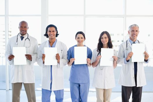 Medical team standing upright holding blank sheets in front of the bright window