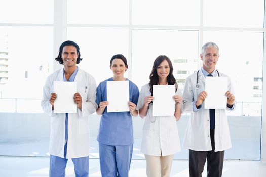Four smiling medical people standing in front of a window while holding blank sheets