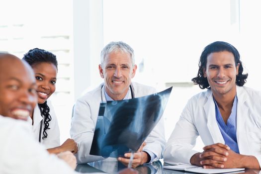 Smiling doctor surrounded by three younger colleagues holding an x-ray of lungs