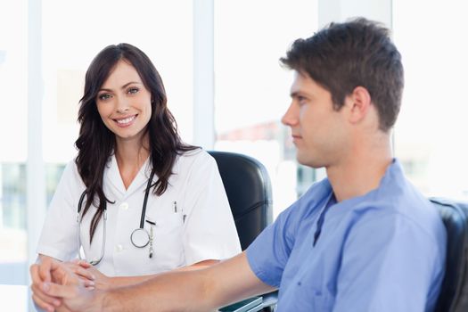 Young female doctor sitting at the desk while looking at her colleague