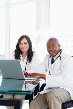 Smiling doctor working hard on a laptop while accompanied by his co-worker