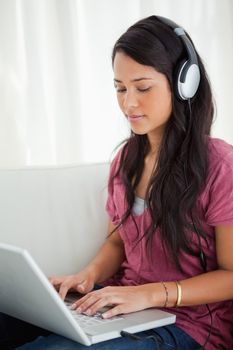 Close-up of a Latino student using a laptop while enjoying music on her sofa