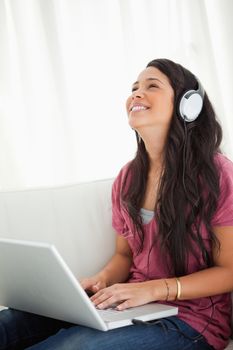 Close-up of a laughing Latino student using a laptop while enjoying music on her sofa