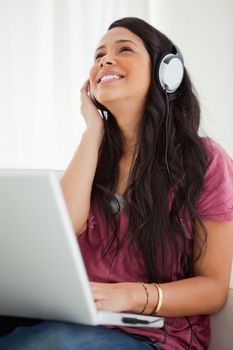 Close-up of a happy Latino student enjoying music with a laptop on her sofa