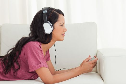 Cute Latino listening to music with her smartphone on a sofa