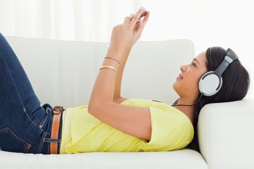 Young Latino woman watching a video with her smartphone while lying on a sofa