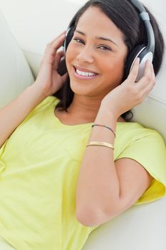 Portrait of a smiling Latino listening music on a smartphone while lying on a sofa