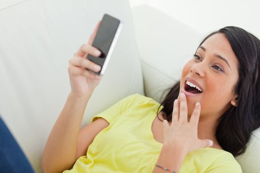 Close-up of a surprised Latino woman looking her smartphone while lying on a sofa