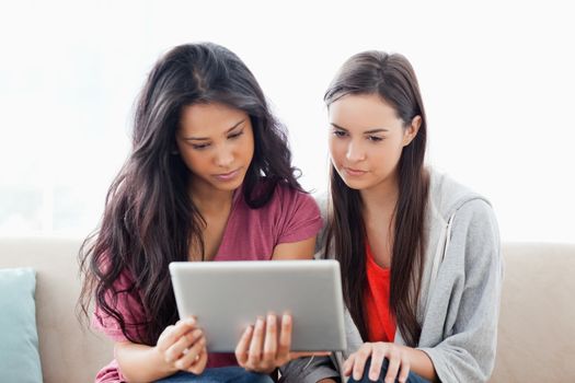 A pair of women on the couch together as they both look at the tablet pc 