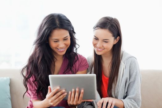 A woman and her friend both watching the tablet pc while on the couch