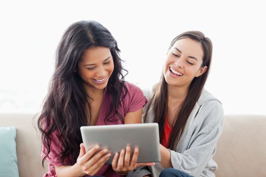 Two women laughing while sitting on the couch together and looking at the tablet pc 