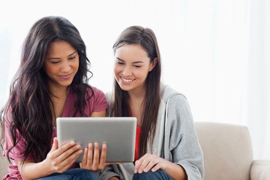 A smiling woman and her friend with a tablet pc as they sit on the couch and watch the screen