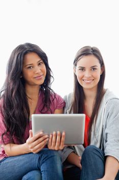 A close up shot of two smiling women looking at the camera and holding a tablet pc