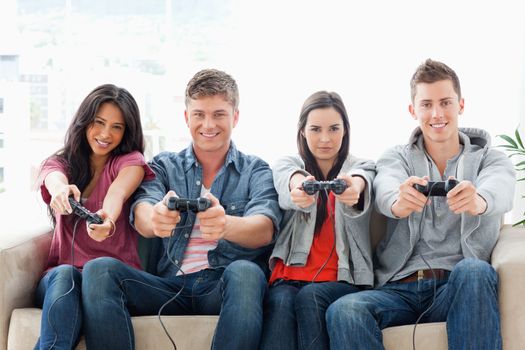 A smiling group of friends sit on the couch together while playing a game with controllers