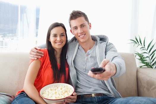 A smiling couple holding each other as they change the channel and look into the camera