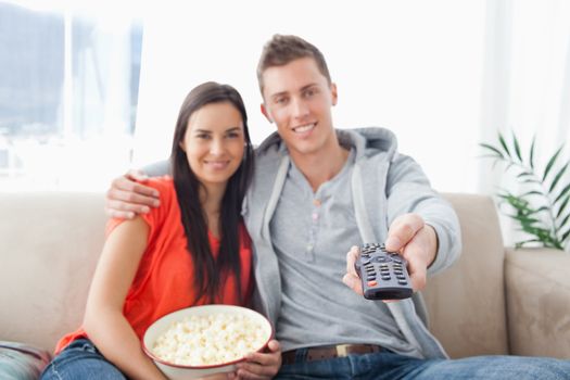 A focused shot on the tv remote on the man's hand as a couple embrace and smile