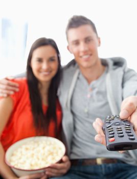 A close up shot focused on the tv remote in the man's hand as he sits with his girlfriend on the couch