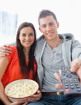 A close up shot with focus on the couple sitting on the couch with popcorn as they use a remote to change the tv