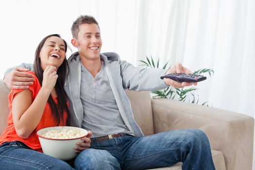 A laughing couple on the couch embracing with popcorn as they watch a tv show 