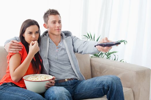 An embracing couple sitting on the couch together as they watch tv and eat popcorn