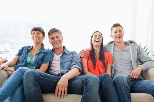 A laughing group of friends look ahead into the camera while on the couch