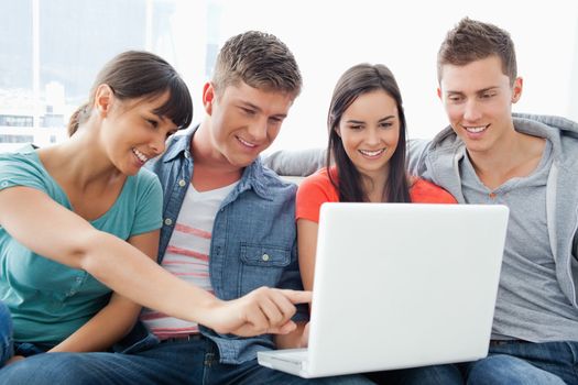 A group of friends smiling as they watch the screen of the laptop with one girl pointing something out 