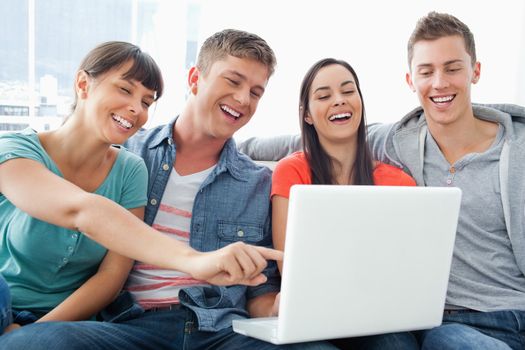 A laughing group of friends around a laptop watching the screen as they sit with one girl pointing the screen