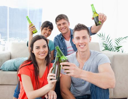 A group of friends indoors celebrating by clinking bottles and toasting 