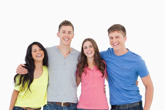 A laughing bunch of friends standing and holding each other as they all look into the camera 