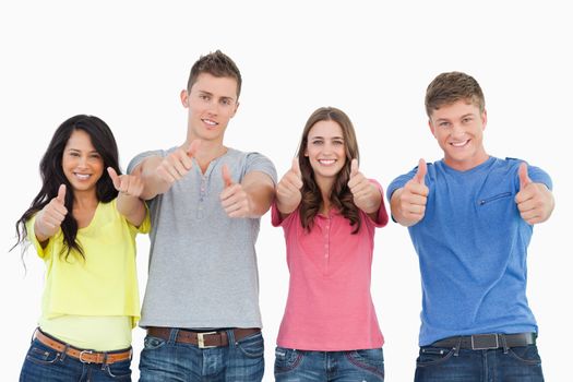 A smiling group of people stand beside each other looking at the camera as they all give thumbs up