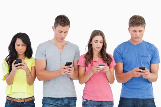 A group of people using their phones and sending texts as they stand beside each other 