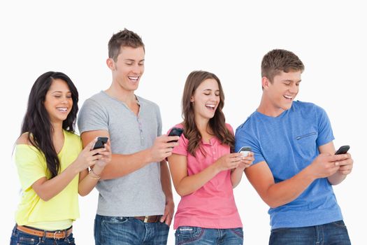 A group of friends laughing as they all send texts with their phones 
