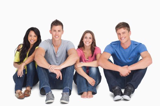 A smiling group of friends sitting beside each other on the ground with their hands on their legs