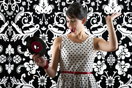 young woman in front of a black and white textured background with 60's inspired style, holding a small record with a red label
