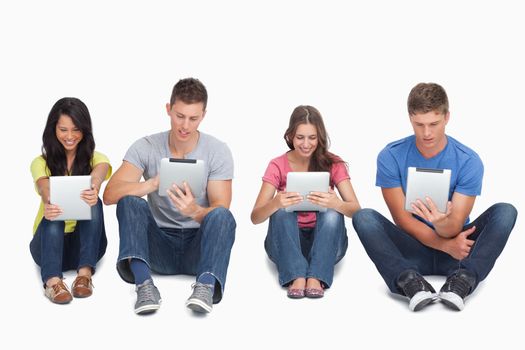 A group of four people sitting beside each other on the ground as they all use their tablet pc's