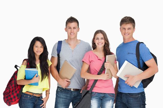 A group of smiling students as they look at the camera while holding notepads and backpacks