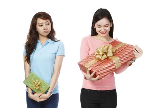 A young woman holding a small gift, envious of the much bigger present of a friend (on white background)