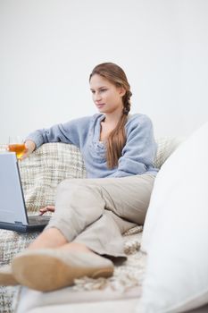 Women sitting and holding a glass while typing on a laptop in a sitting room