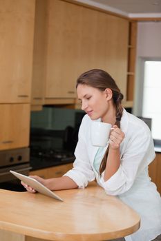 Woman holding a cup while looking at a tablet computer in a kitchen