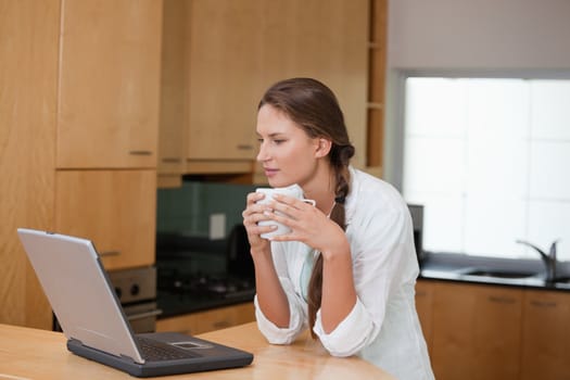 Woman holding a cup while looking at a computer in a kitchen