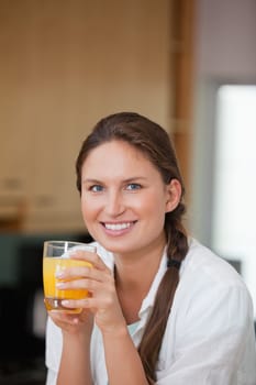 Woman drinking orange juice while smiling in a kitchen