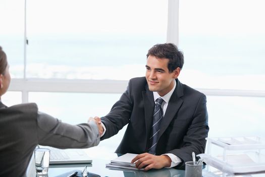 Businessman shaking hands with a client while sitting in an office