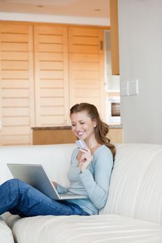 Woman using a laptop while holding a card in a sitting room