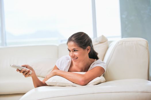 Woman lying on a sofa while holding a remote in a sitting room