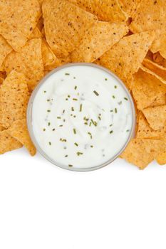 Close up of a bowl of dip with herbs surrounded by nachos against a white background